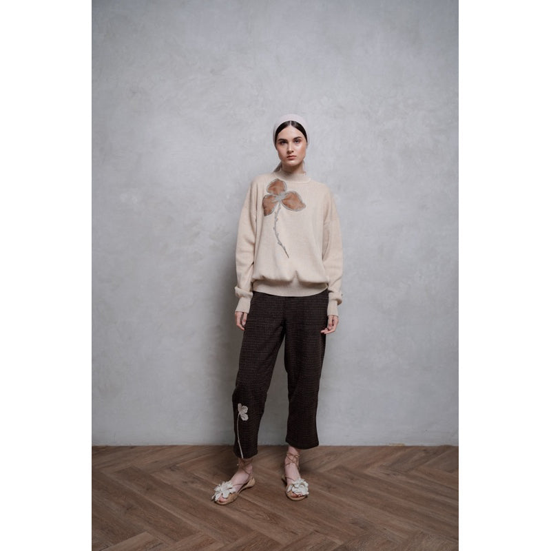 A person standing against a neutral background, wearing a brown long-sleeve sweater by Glashka with a floral design.