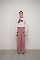 A person standing against a neutral background, wearing a pink long-sleeve sweater by Glashka with a floral design.