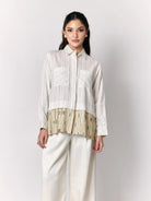 Woman wearing a white shirt with a textured green panel by Studio Tui and white pants on a light gray background