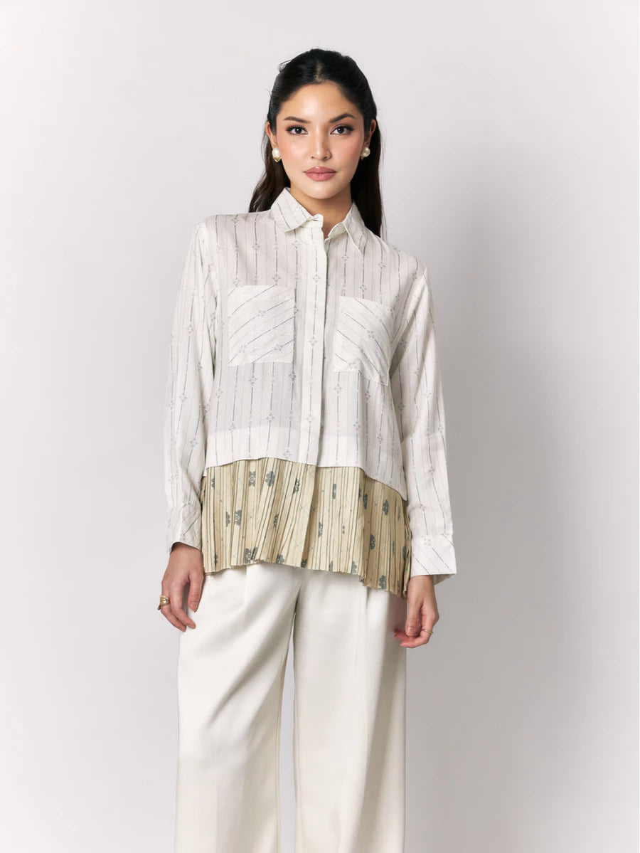 Woman wearing a white shirt with a textured green panel by Studio Tui and white pants on a light gray background