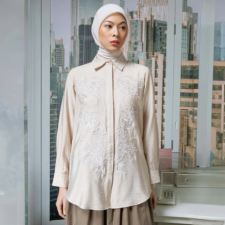 Woman wearing a beige embroidered shirt by Hijabchic with a cityscape in the background