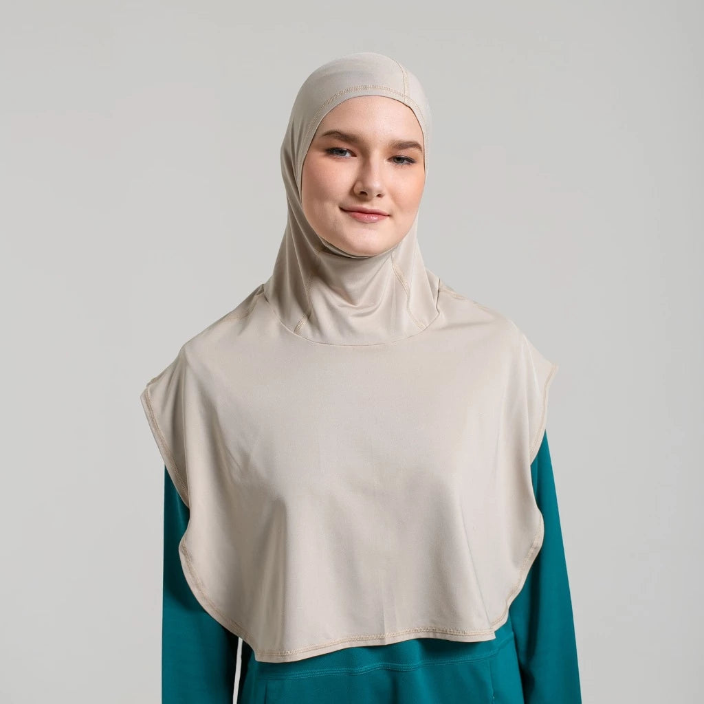 Woman wearing a beige sport hijab by Noore and teal top against a light gray background