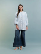 Woman wearing a light blue blouse by Kasa Heritage and blue jeans against a light gray background