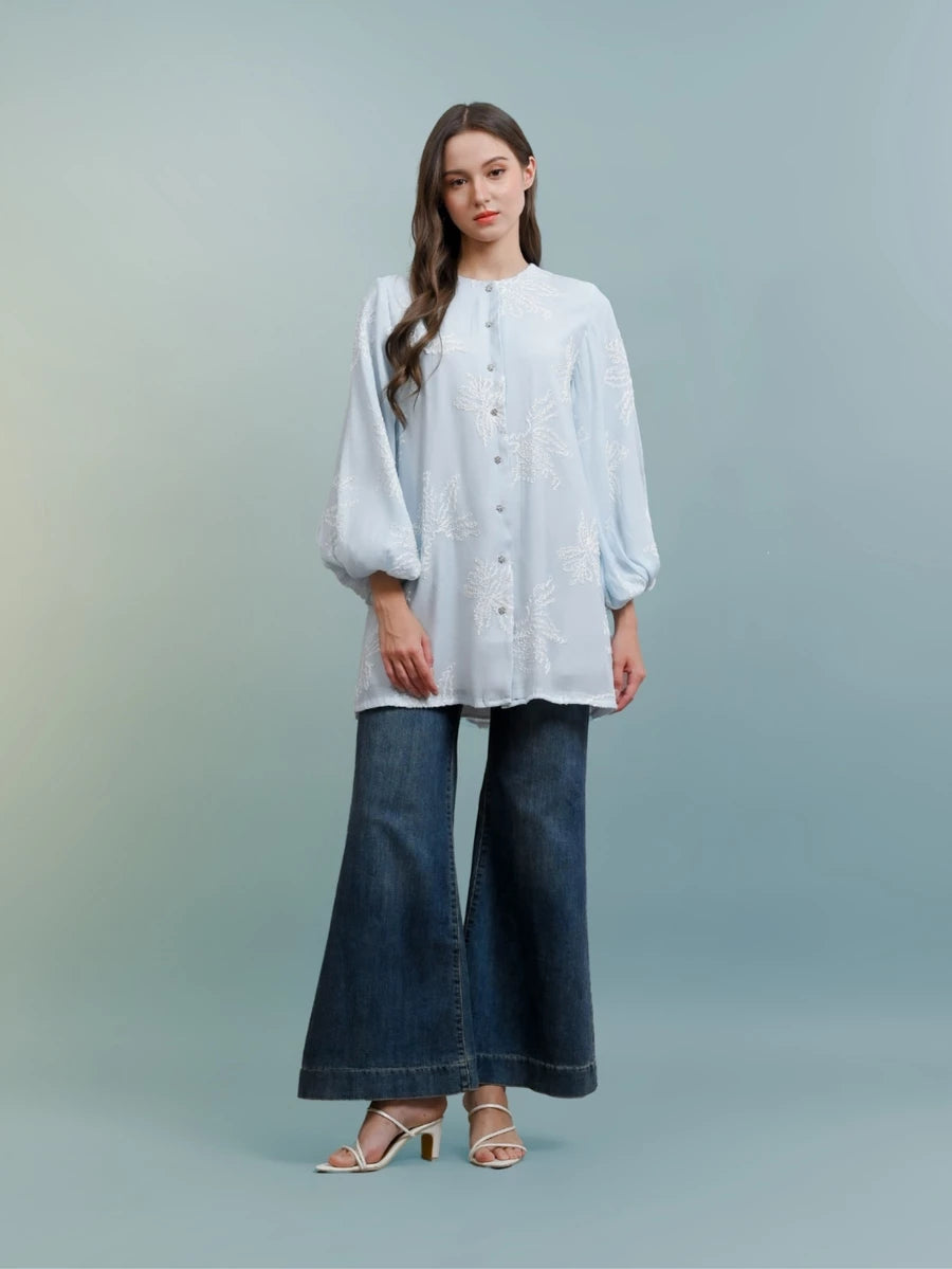 Woman wearing a light blue blouse by Kasa Heritage and blue jeans against a light gray background
