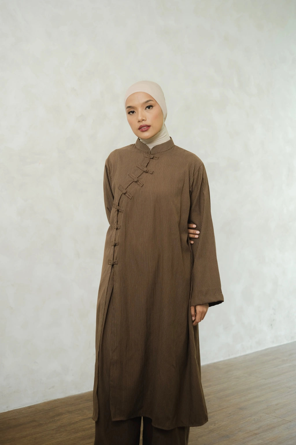 Woman wearing a brown long-sleeve tunic by Tufine and pants with a beige hijab against a white wall.

Seorang wanita mengenakan tunik lengan panjang berwarna cokelat dari Tufine dan celana panjang, serta hijab berwarna krem, dengan latar belakang dinding putih.