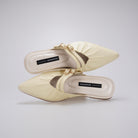 A pair of butter yellow-colored pointed-toe mule sandals by Cekhas with gold-tone hardware and a strap detail, shown from a top-down view on a light gray background.