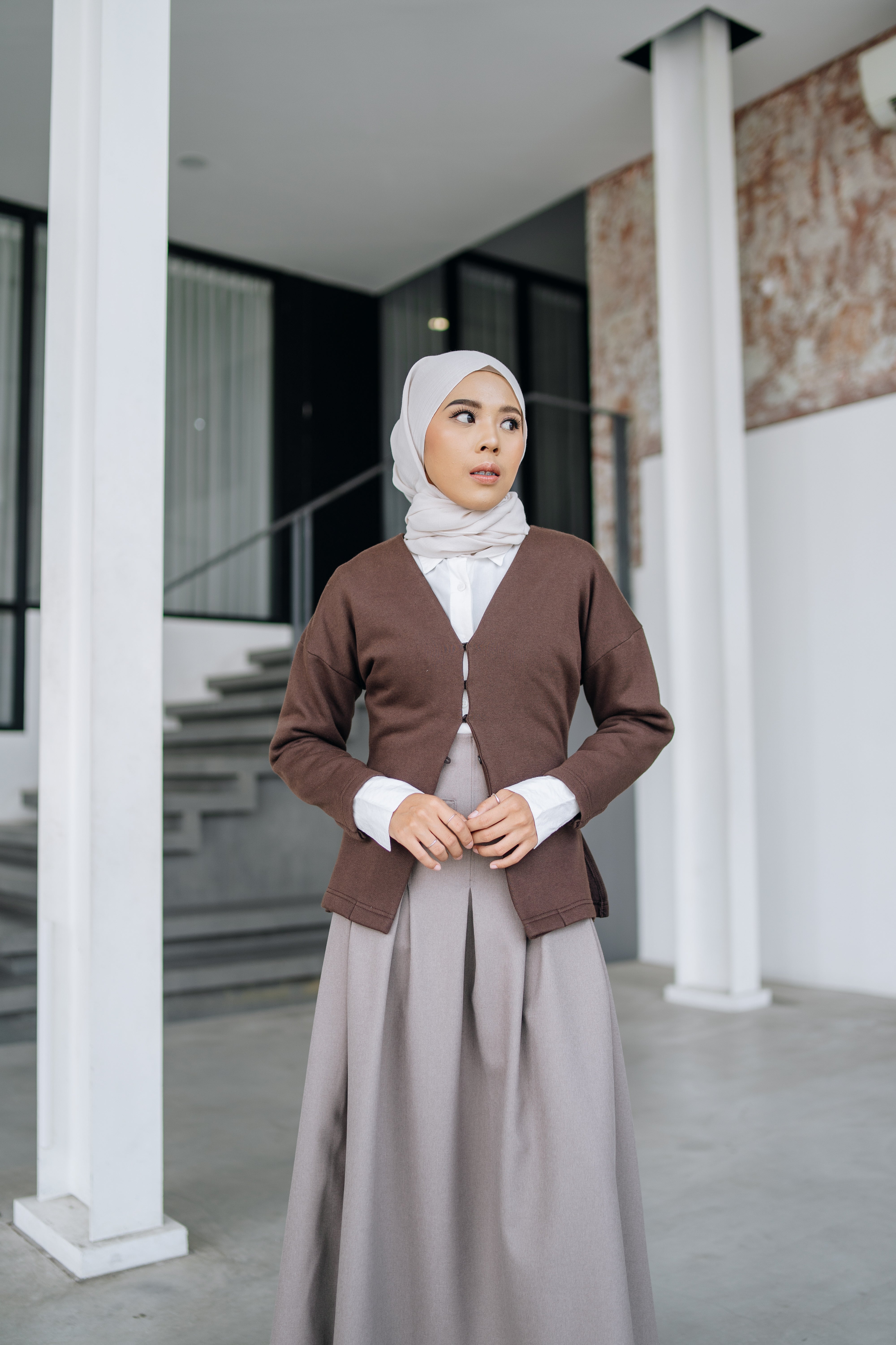 A woman wearing a fitted cardigan in a coffee color by Swifter, paired with a hijab, standing indoors.