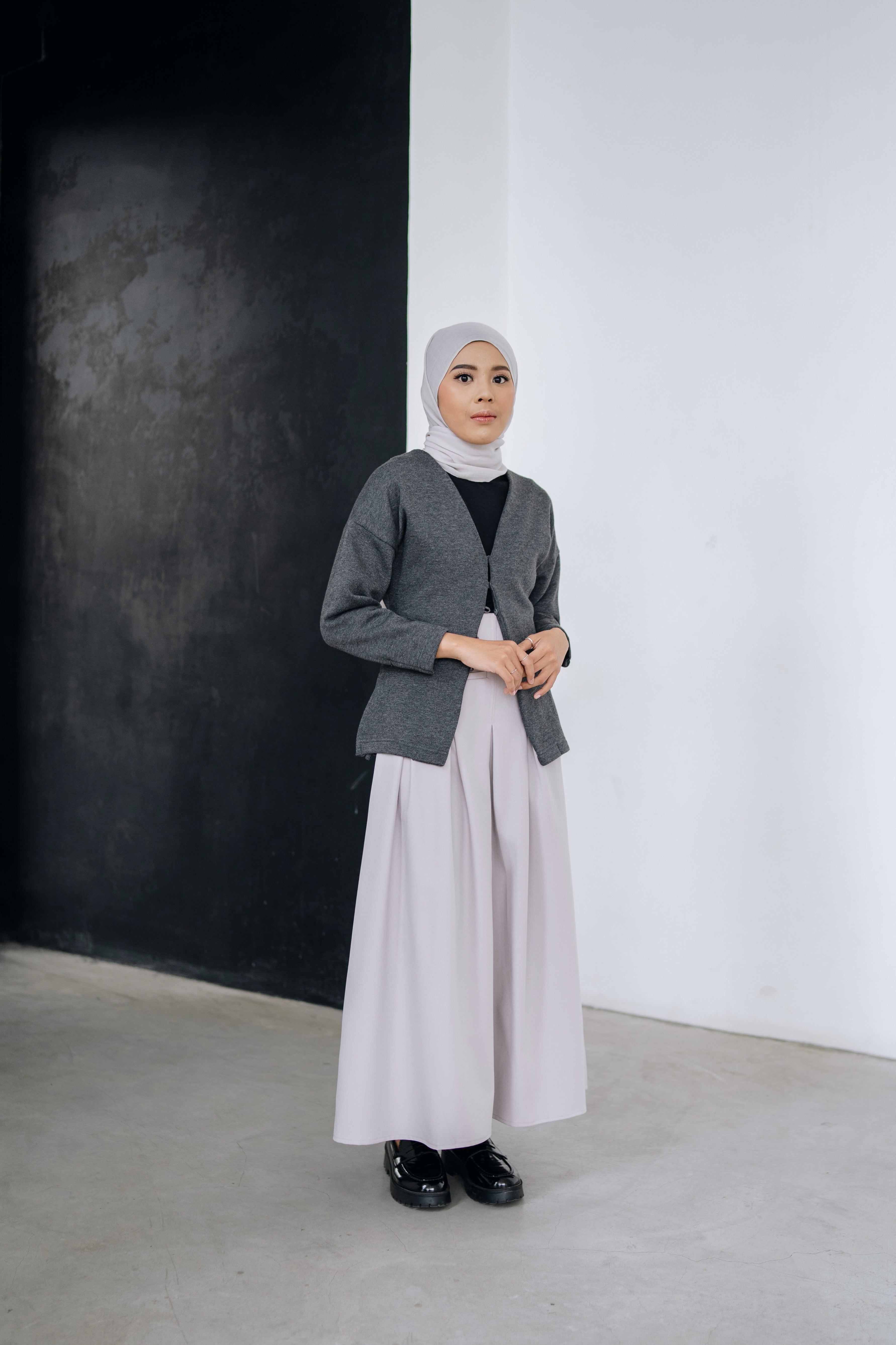 A woman wearing a fitted cardigan in a dark grey color by Swifter, paired with a hijab, standing indoors.