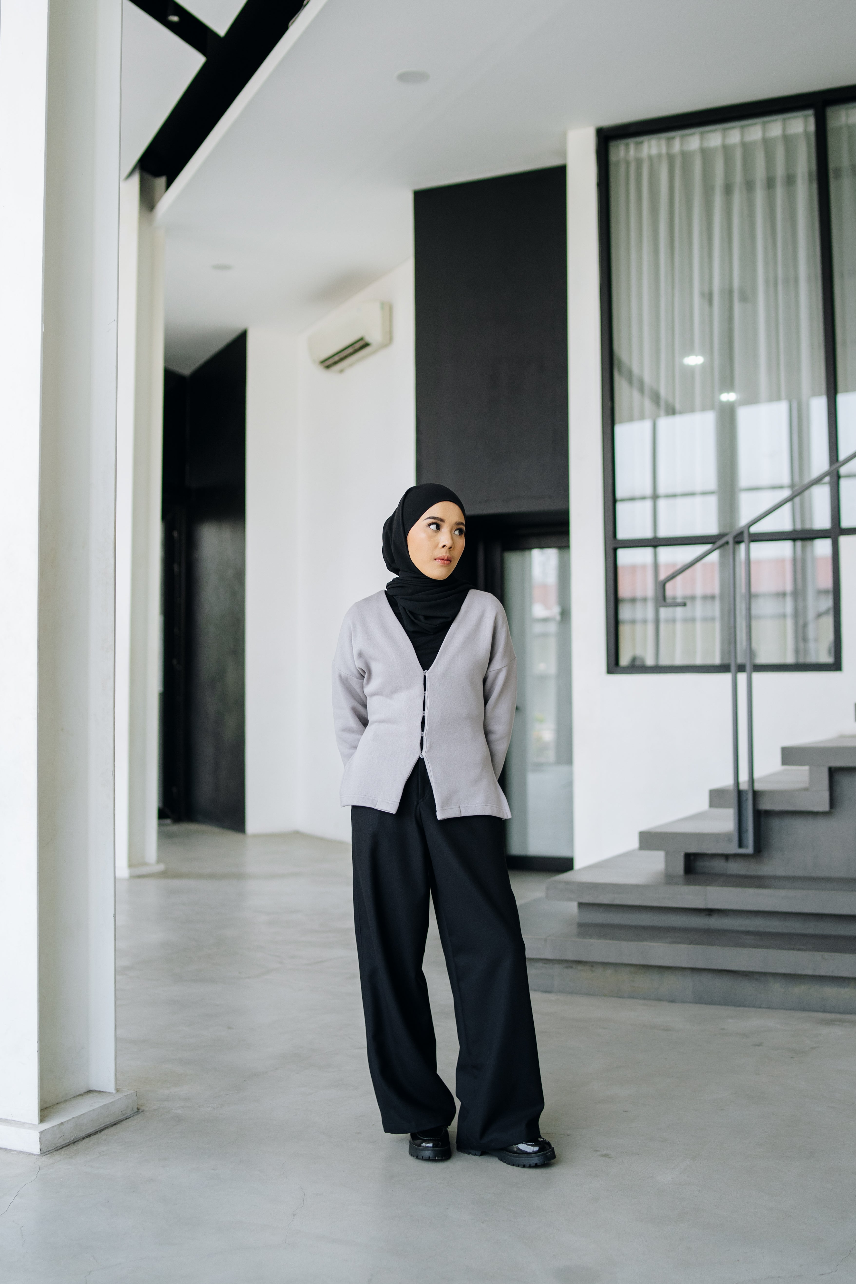 A woman wearing a fitted cardigan in a grey color by Swifter, paired with a hijab, standing indoors.