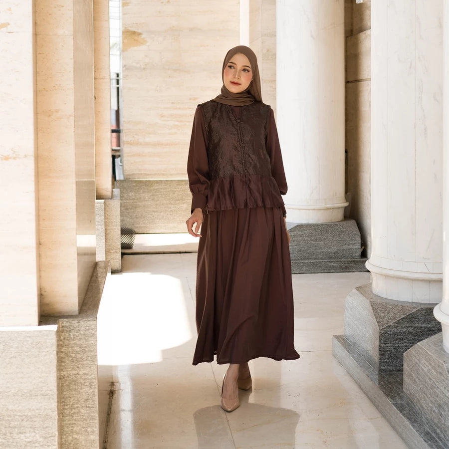 Woman in a brown ceremonial dress by Tunique standing in a marble hallway