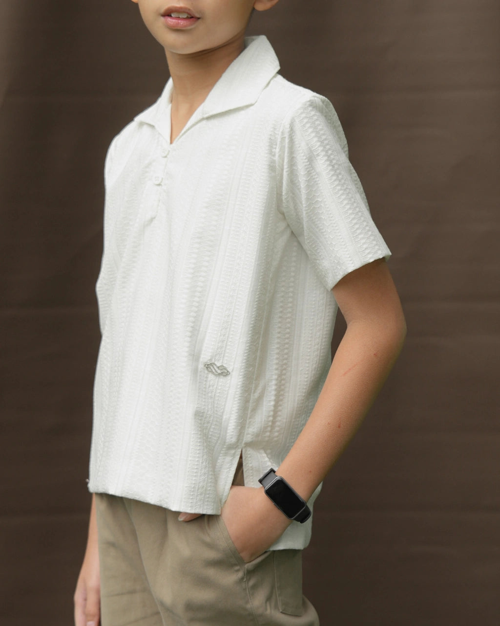 Child wearing a white textured shirt by Mistyvori and beige pants against a brown background