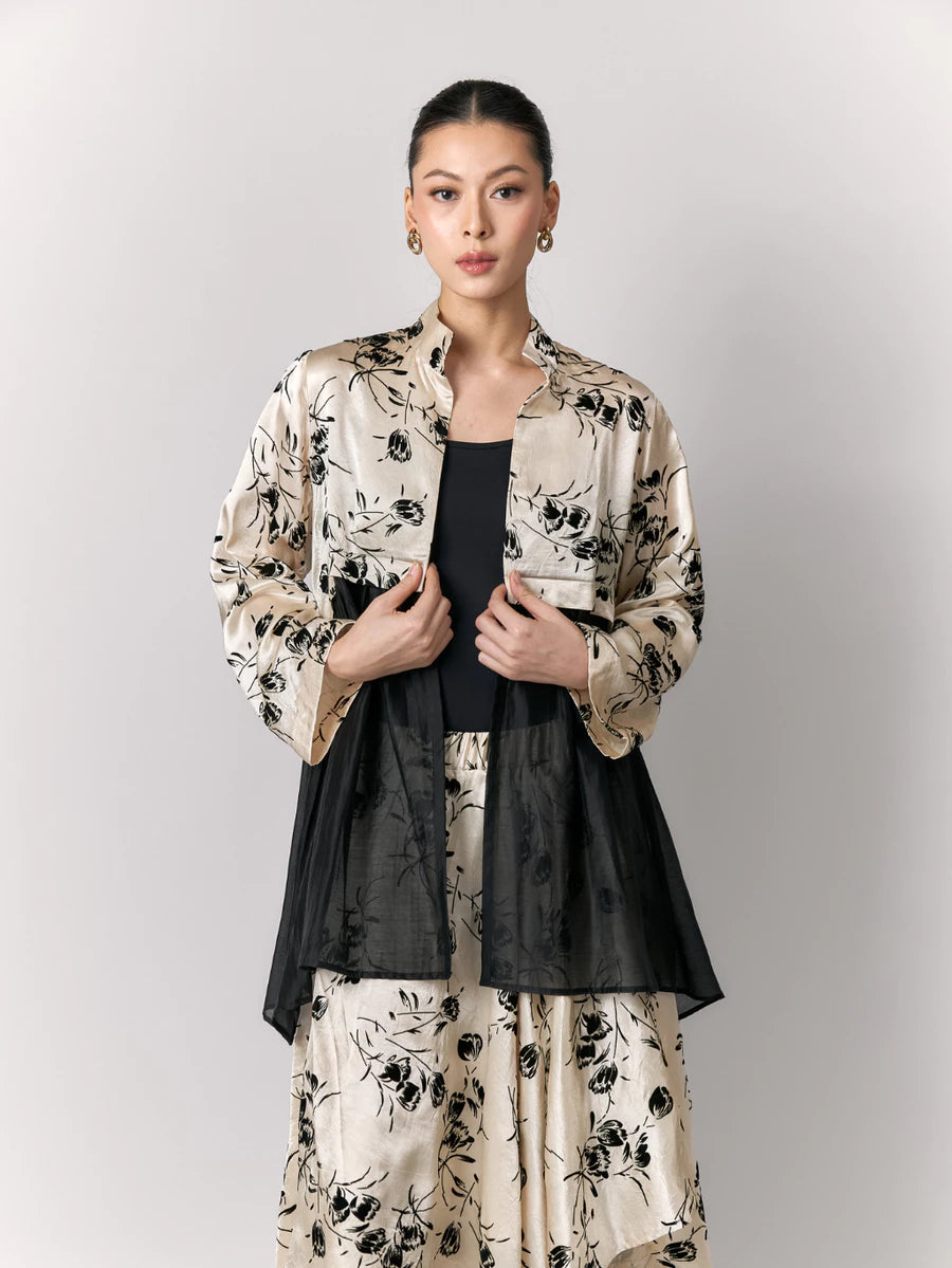 Woman wearing a floral jacket by Studio Tui over a black top and skirt on a gray background