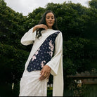 A woman wearing a traditional white blouse by Kartinis Label with asymmetrical batik design on the yoke, featuring floral patterns and bead details.