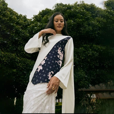 A woman wearing a traditional white blouse by Kartinis Label with asymmetrical batik design on the yoke, featuring floral patterns and bead details.