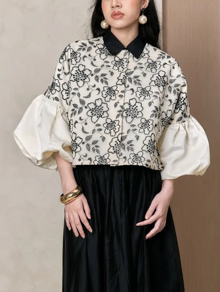 Woman wearing a floral puffy shirt with white sleeves and a black skirt against a beige background