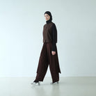Person wearing a brown top and barrel pants by Rashawl with a black hijab on a white background