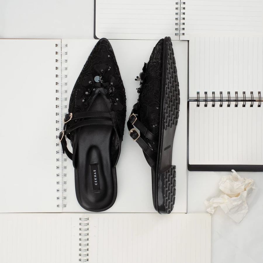 Black pointed-toe mules sandals by Cekhas on a white surface with a notebook