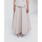 A woman wearing a cream Sienna skirt with soft pleats by Kasyalia, paired with a matching top. The skirt reaches down to the ankles and has a flowing silhouette.