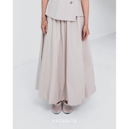 A woman wearing a cream Sienna skirt with soft pleats by Kasyalia, paired with a matching top. The skirt reaches down to the ankles and has a flowing silhouette.