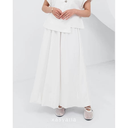 A woman wearing a white Sienna skirt with soft pleats by Kasyalia, paired with a matching top. The skirt reaches down to the ankles and has a flowing silhouette.