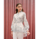 Woman wearing a floral blue blouse by Kasa Heritage and white pants against a pink curtain background
