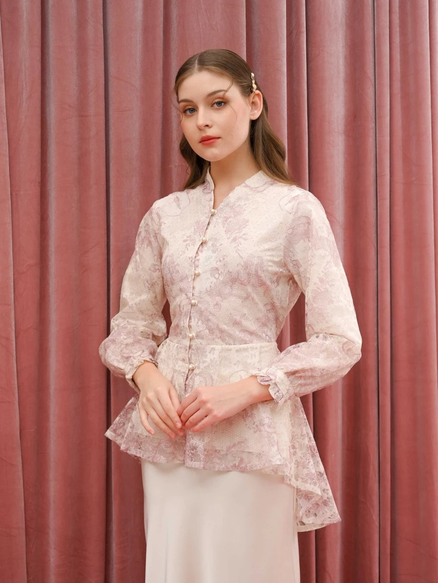 Woman wearing a light pink floral blouse by Kasa Heritage and white pants against a pink curtain background