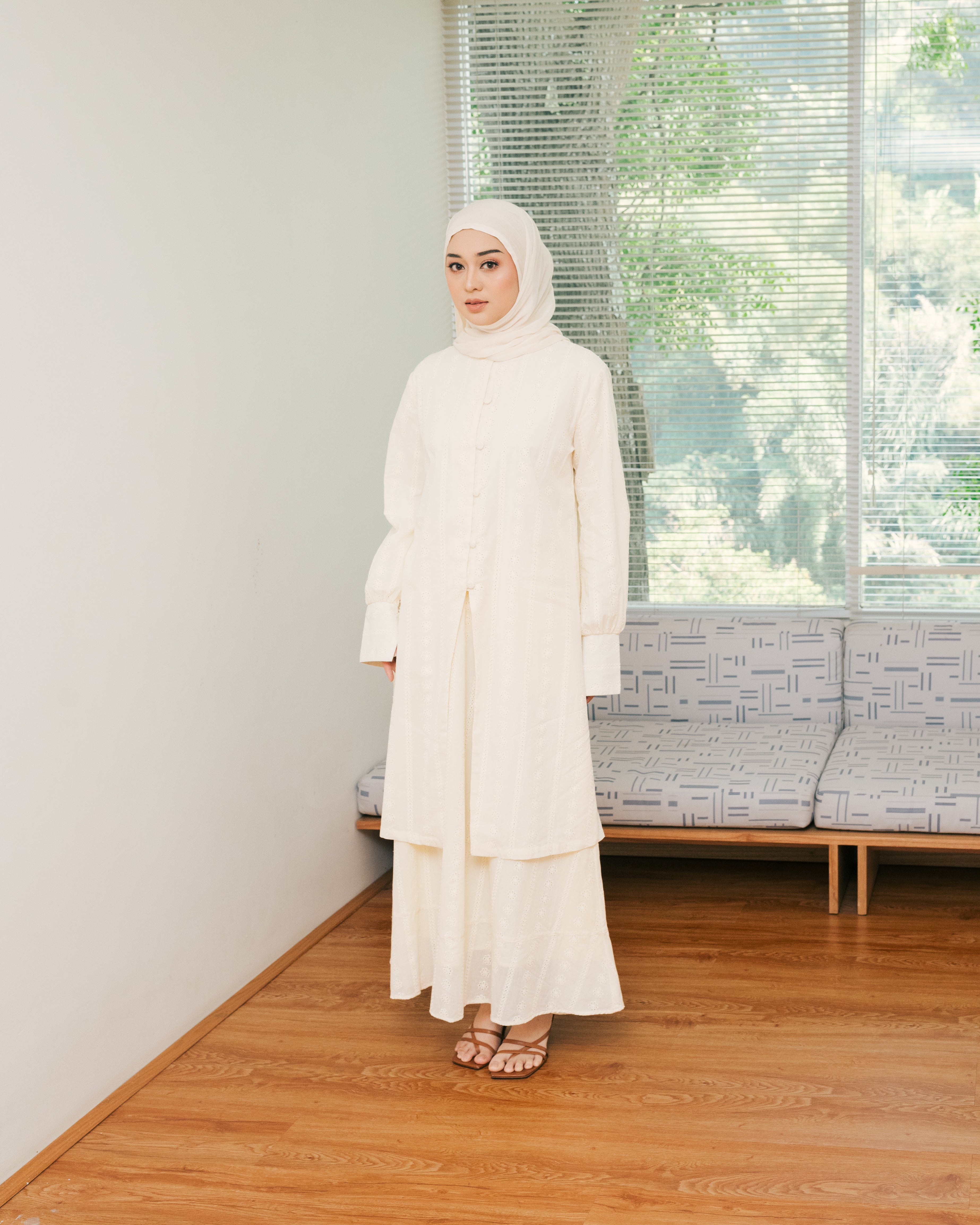 Woman in a ivory-colored top and skirt from Atala Scarves standing in a room with wooden flooring and a window in the background.