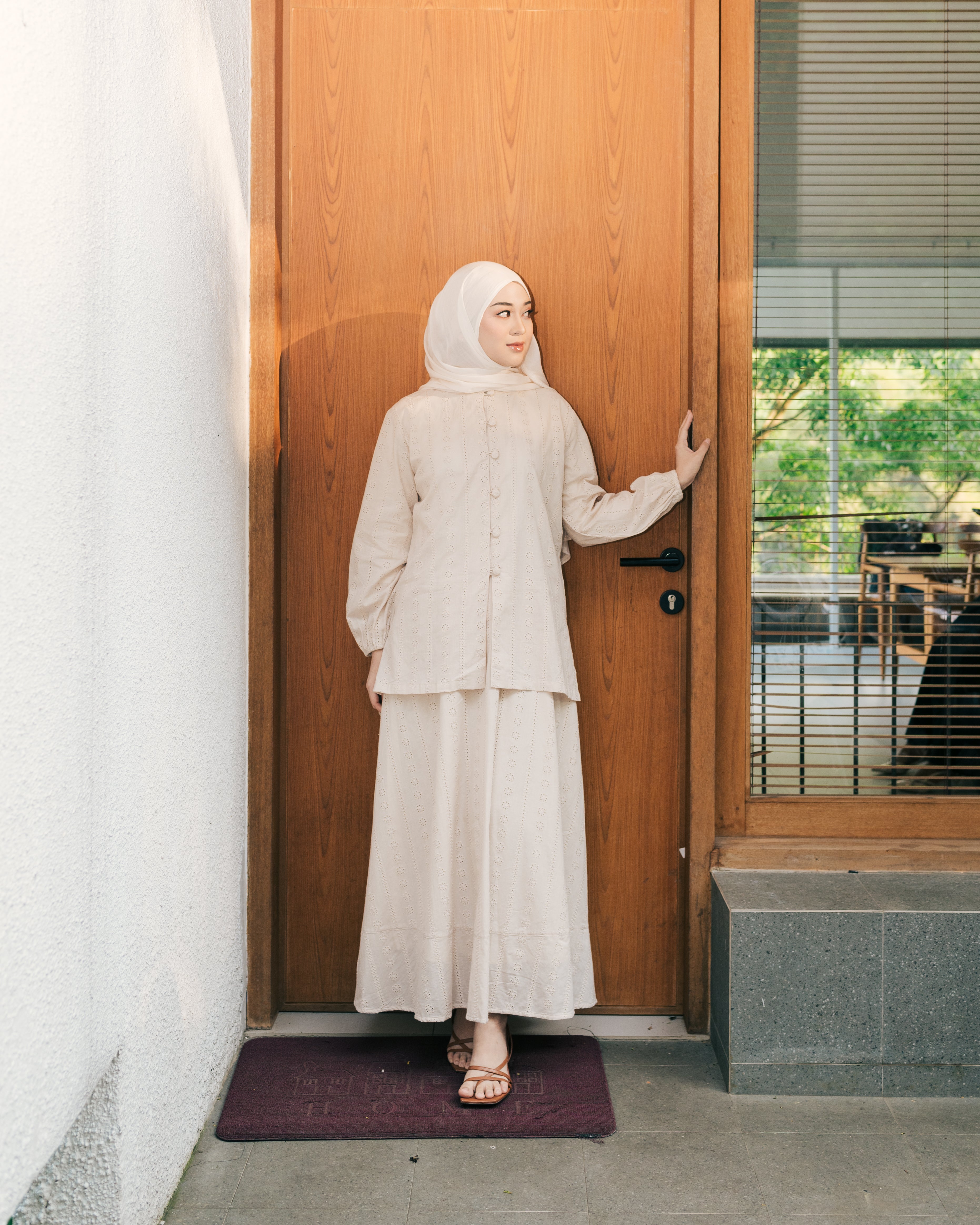 Woman in a nude-colored top and skirt from Atala Scarves standing in front of a wooden door.