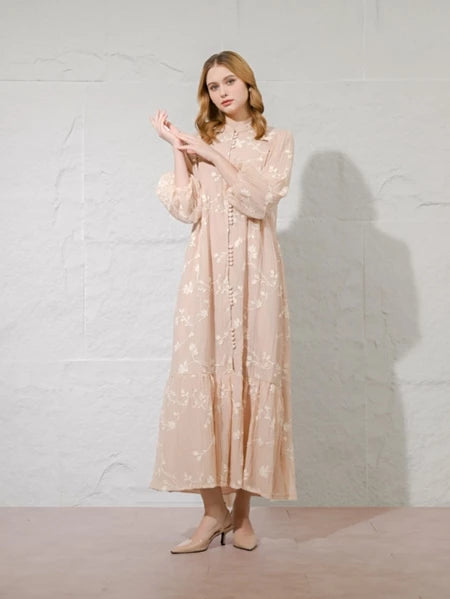 Woman wearing a long, light-colored dress with floral patterns by Kasa Heritage against a plain background