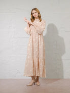 Woman wearing a long, light-colored dress with floral patterns by Kasa Heritage against a plain background