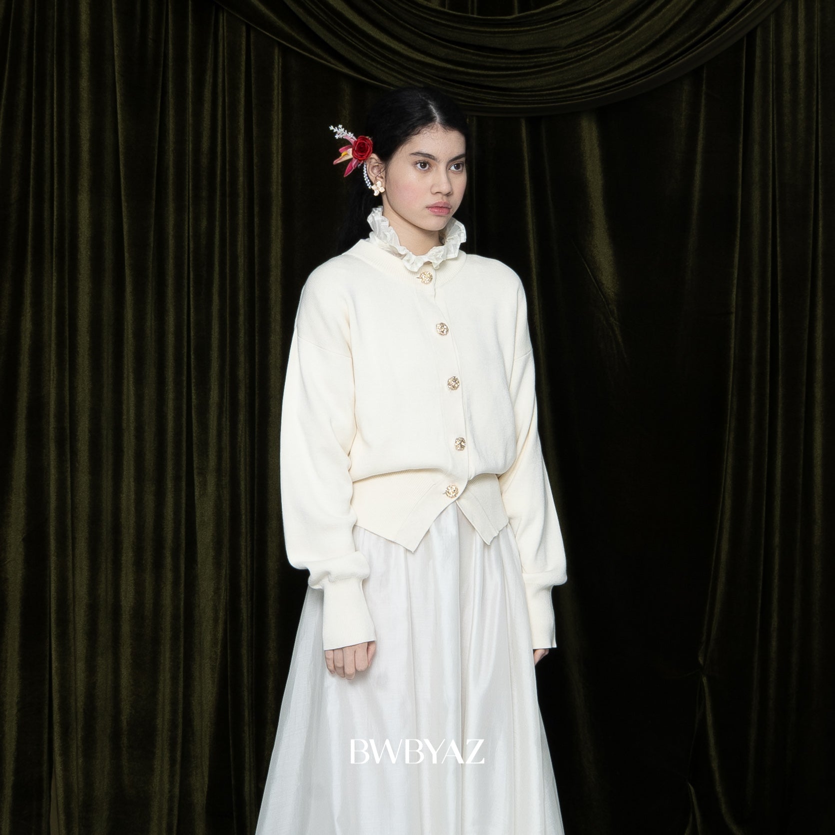 Woman wearing a white fit knitted sweater by BWBYAZ with a floral headpiece against a black curtain backdrop.