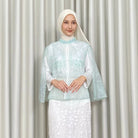 Woman wearing a light blue embroidered vest by Kartinis Label and white skirt against a plain background