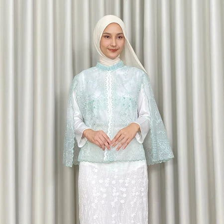 Woman wearing a light blue embroidered vest by Kartinis Label and white skirt against a plain background