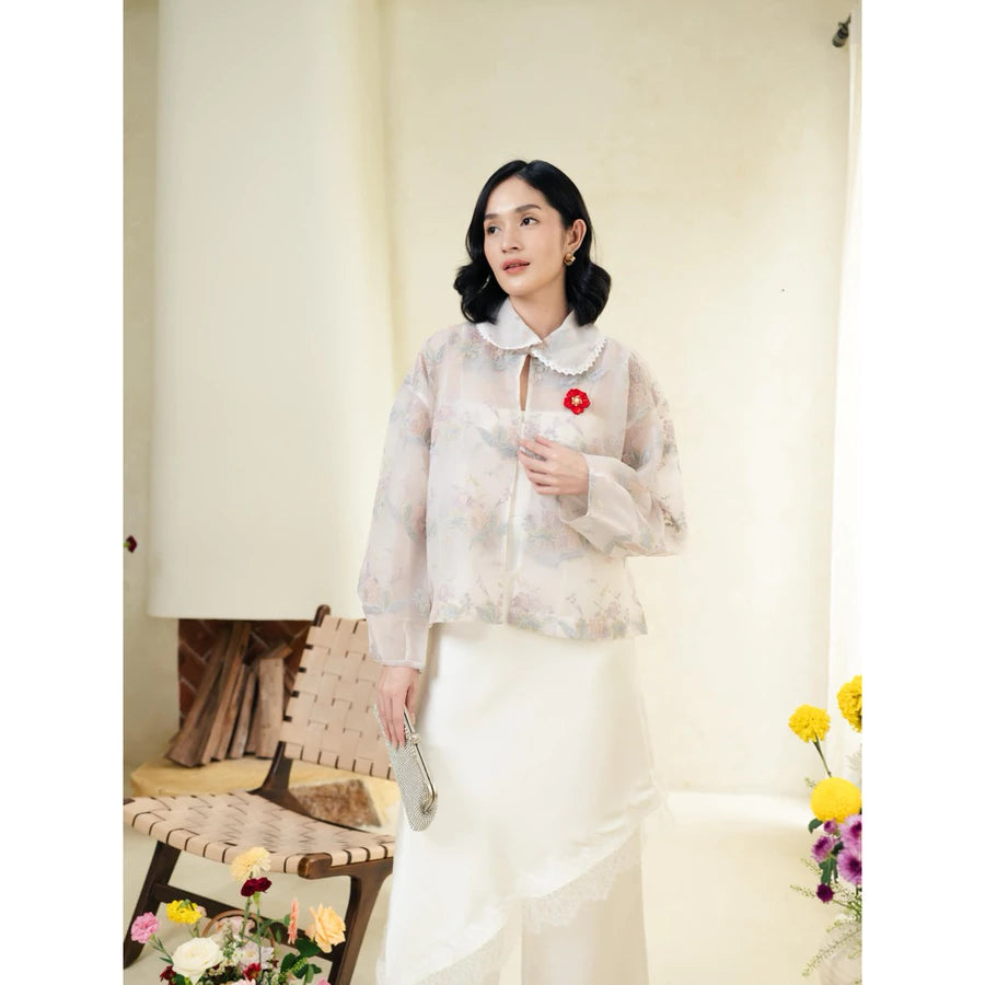 Woman wearing a blue lace outer with floral details by Haidee Orlin, with flowers and furniture around.
