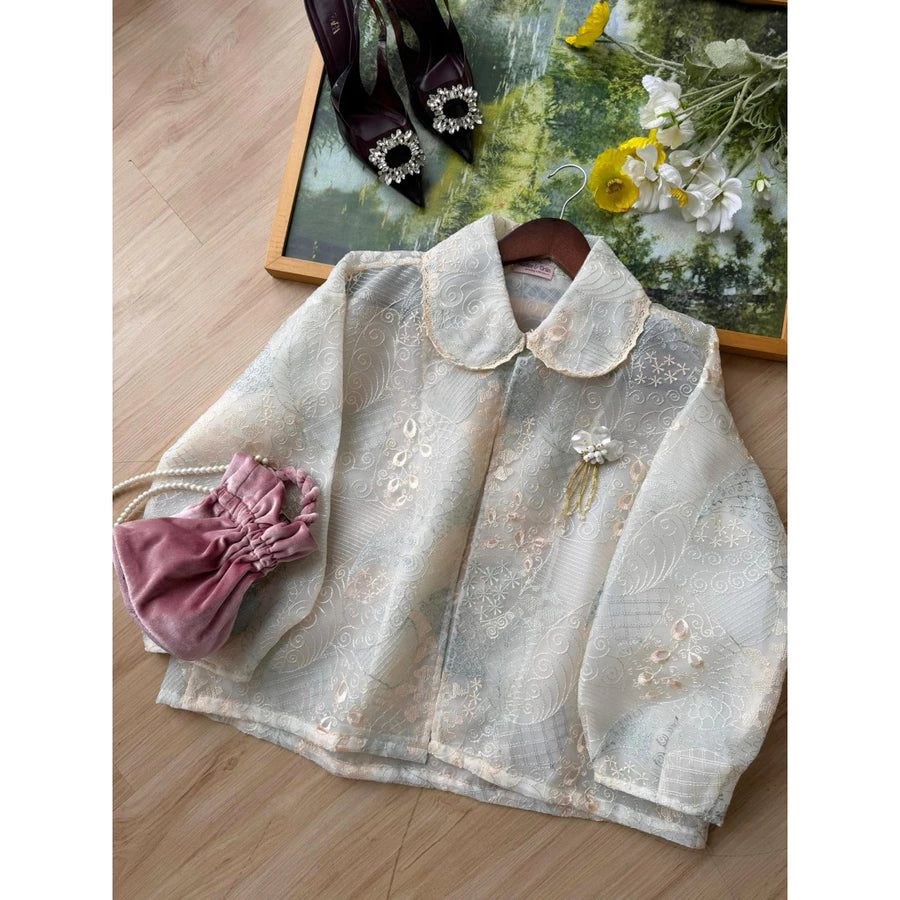 Peach-grey-colored embroidered lace outer by Haidee Orlin on a wooden surface with decorative items.