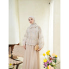 Woman wearing a pink lace outer with floral details by Haidee Orlin with a hijab standing indoors next to a chair and flowers.