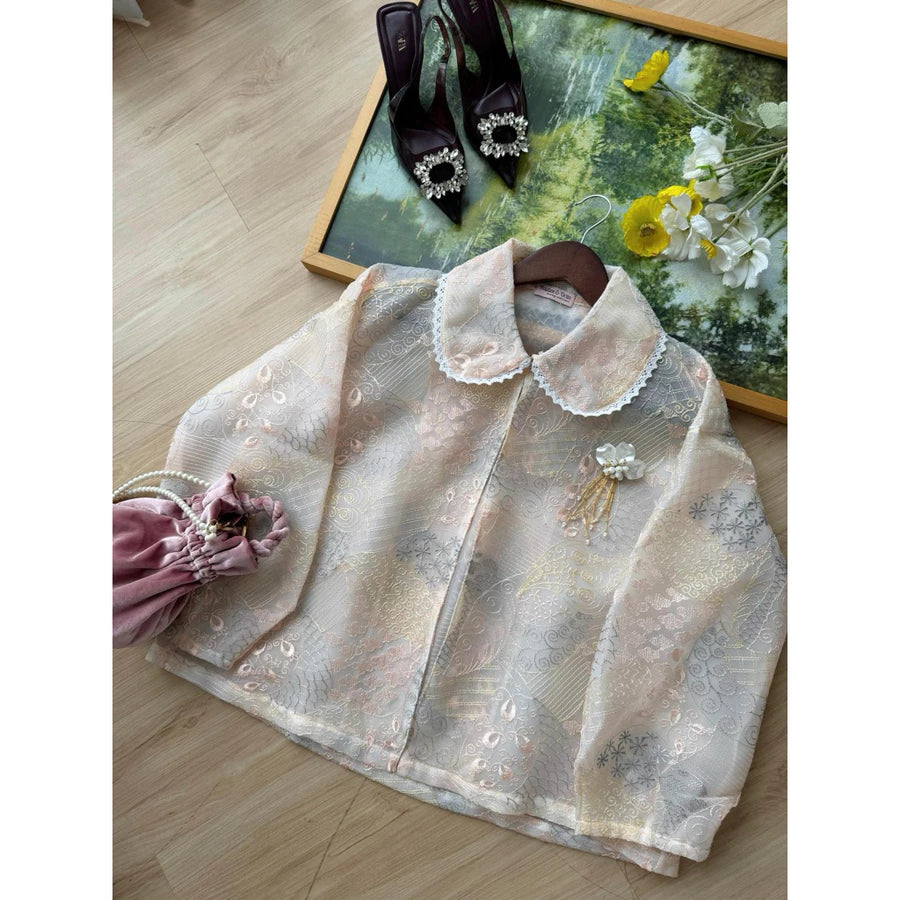 Light-colored lace outer by Haidee Orlin on a wooden floor with decorative shoes and flowers in the background.