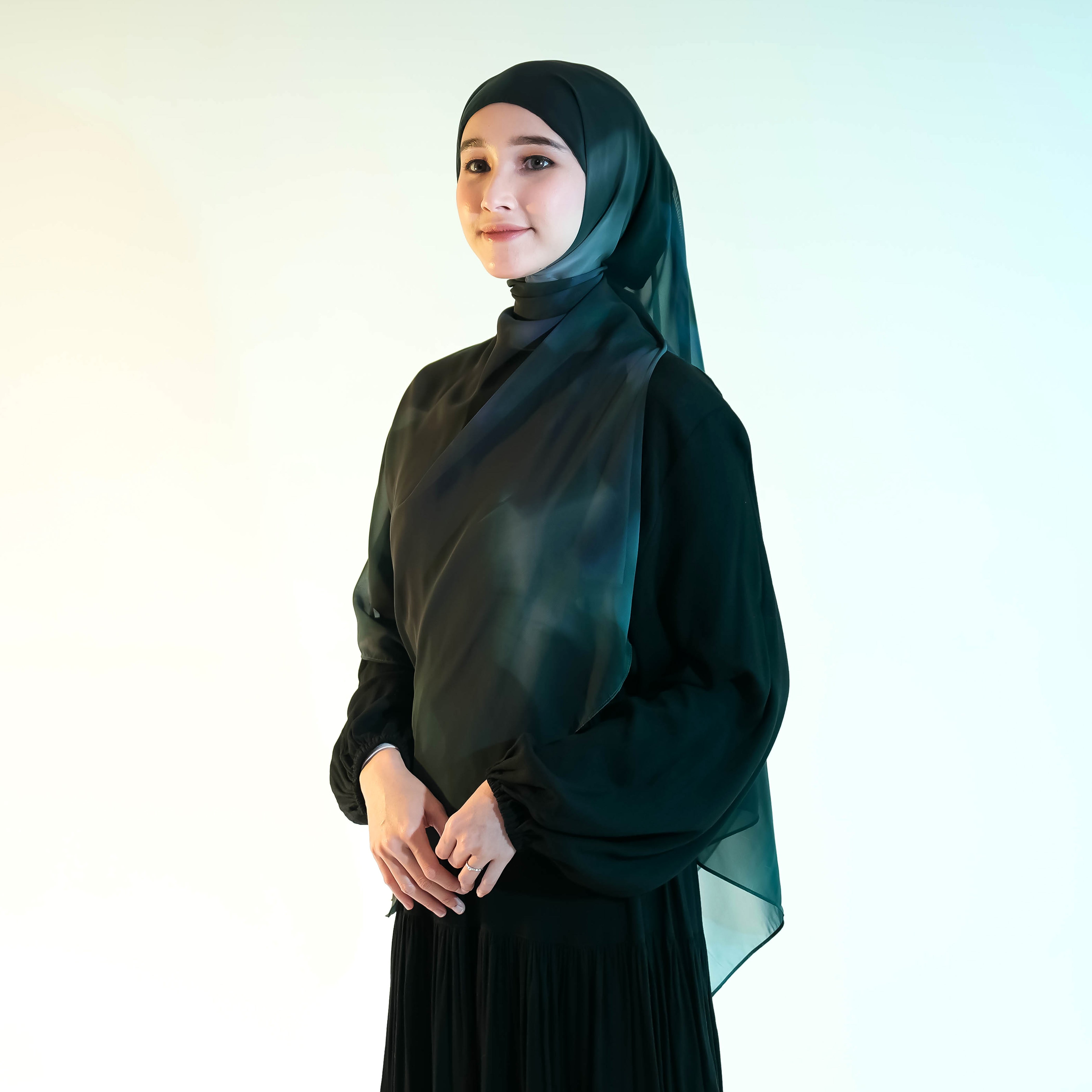 Woman wearing a dark green pashmina hijab by Puru Kambera and dress against a white background
