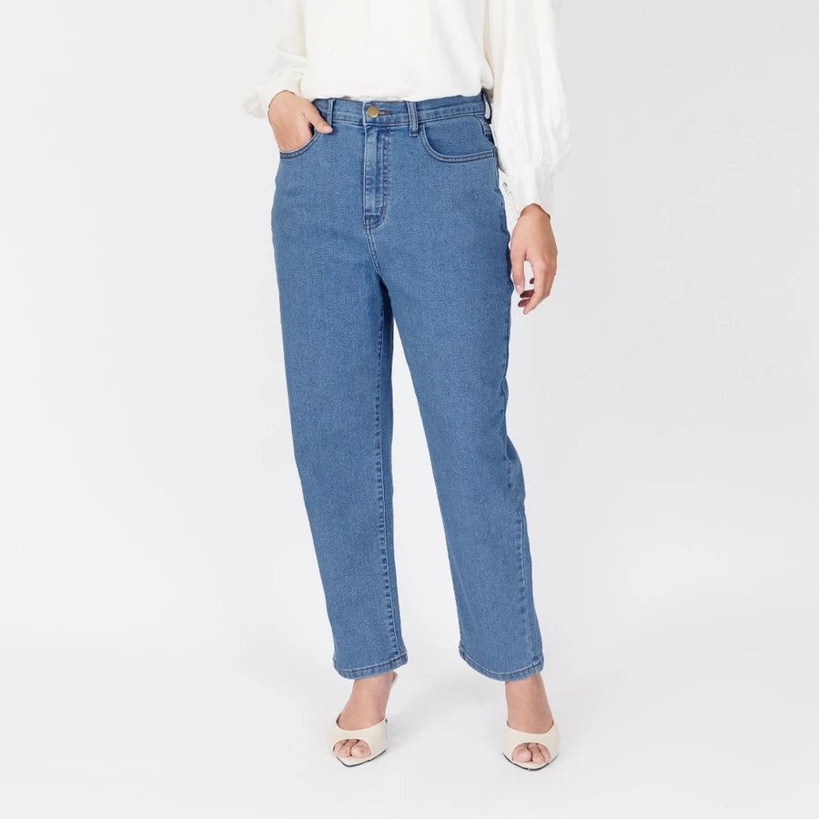 A model wearing medium-wash blue straight-leg denim pants, styled with a white long-sleeve blouse and white heeled sandals, photographed against a clean white studio background.

Seorang model yang mengenakan celana denim lurus berwarna biru dengan warna medium-wash, dipadukan dengan blus lengan panjang berwarna putih dan sandal bertumit putih, difoto dengan latar belakang studio berwarna putih bersih.