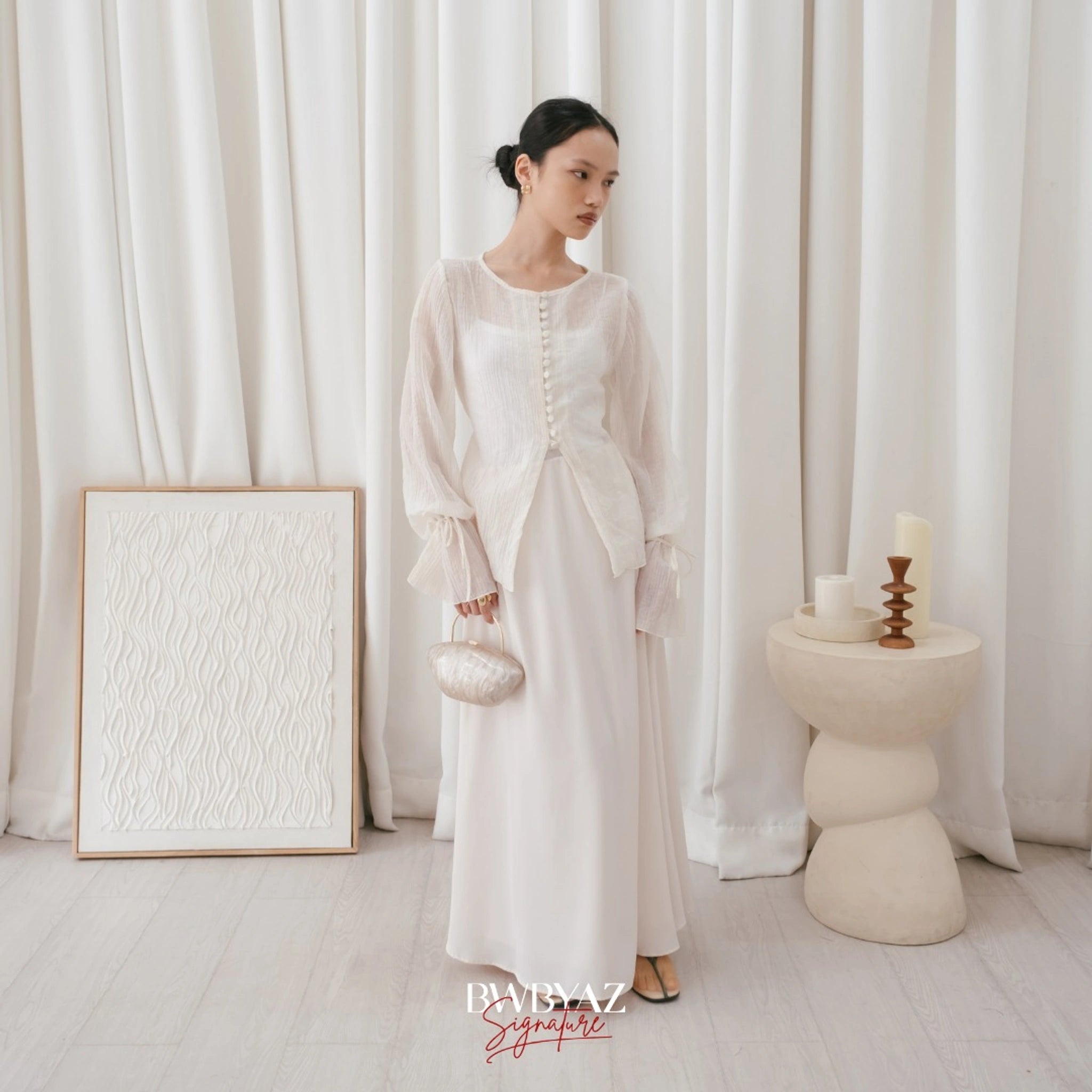 A woman wearing a white, long-sleeved blouse with front buttons and a waist tie from BWBYAZ, paired with a white skirt.