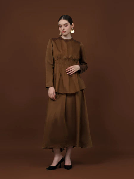 Woman wearing a brown long-sleeve soft lyocell top designed with pleats, a fitted waist, and puffy shoulders.
