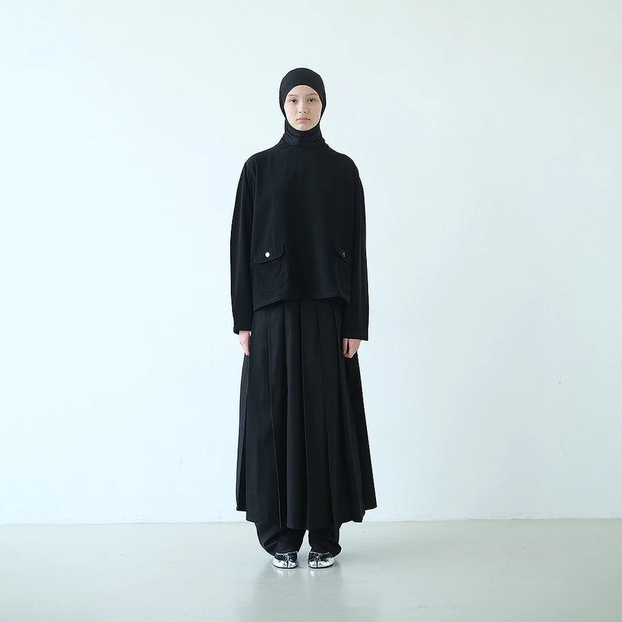 Person wearing a black top and skirt by Rashawl with a headscarf on a white background
