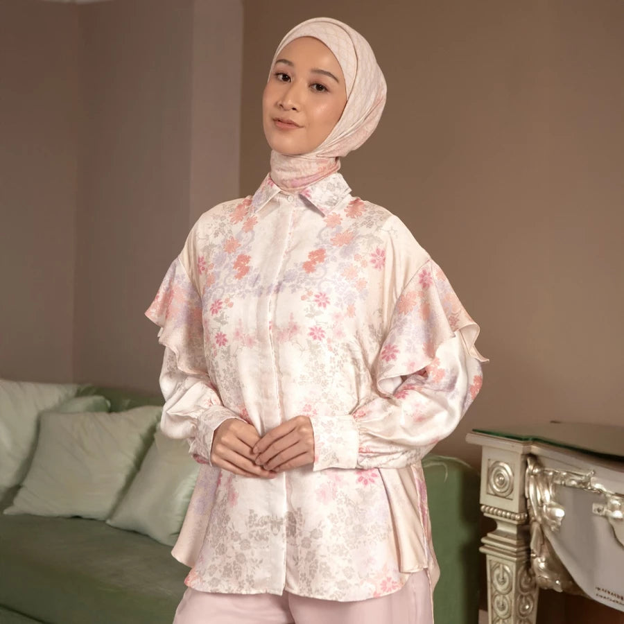 Woman wearing a peach-colored floral shirt by Hijabchic and hijab in a room with a couch and decorative items.