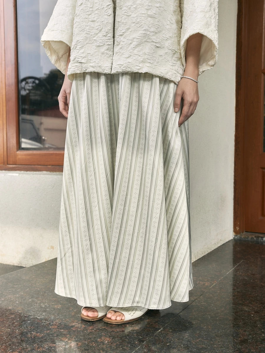 Person wearing a light-colored outfit with a striped skirt by Studio Tui standing indoors.