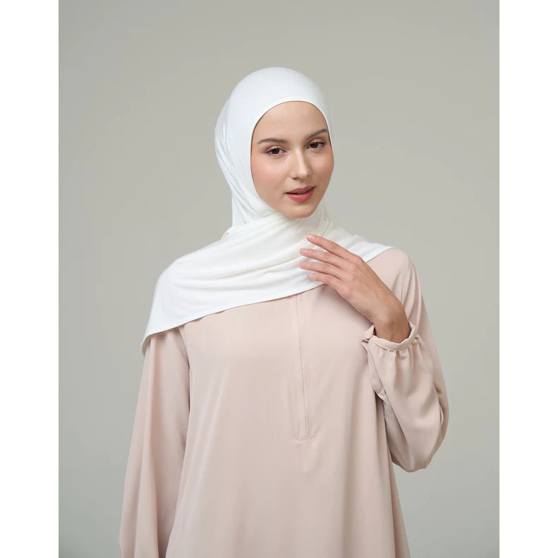 Woman wearing a white hijab by Inanna and beige top against a gray background