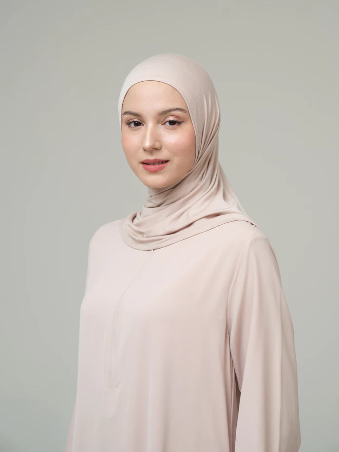 Woman wearing a cream-colored hijab by Inanna and dress against a gray background