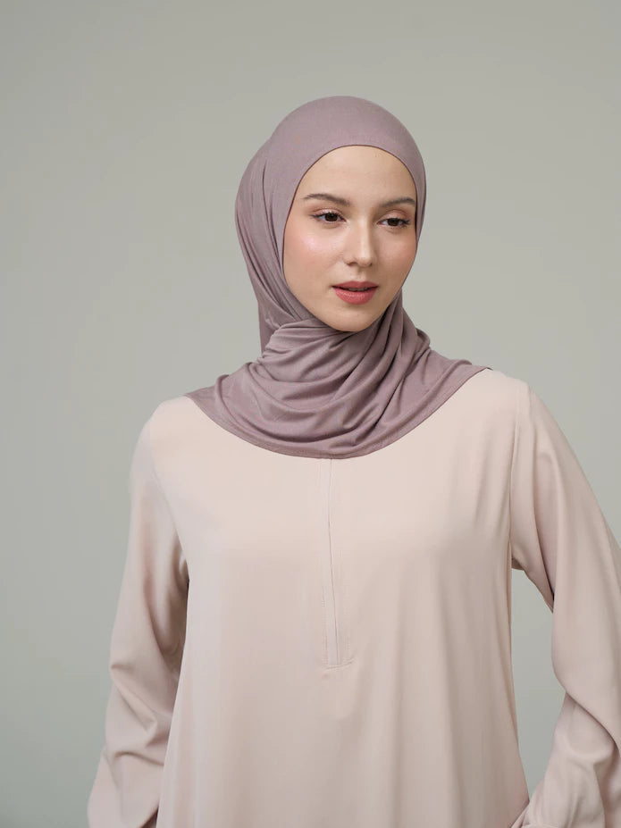 Woman wearing a dark purple hijab by Inanna and beige top against a gray background