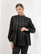 A woman wearing a black Valca Blouse by Kasa Heritage with long sleeves and a round neckline, made of silk, with a visible textured pattern.