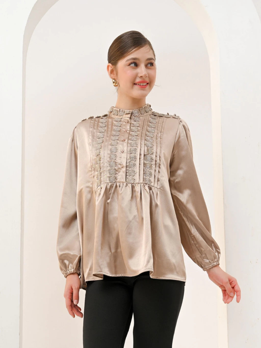 A woman wearing a brown Valca Blouse by Kasa Heritage with long sleeves and a round neckline, made of silk, with a visible textured pattern.