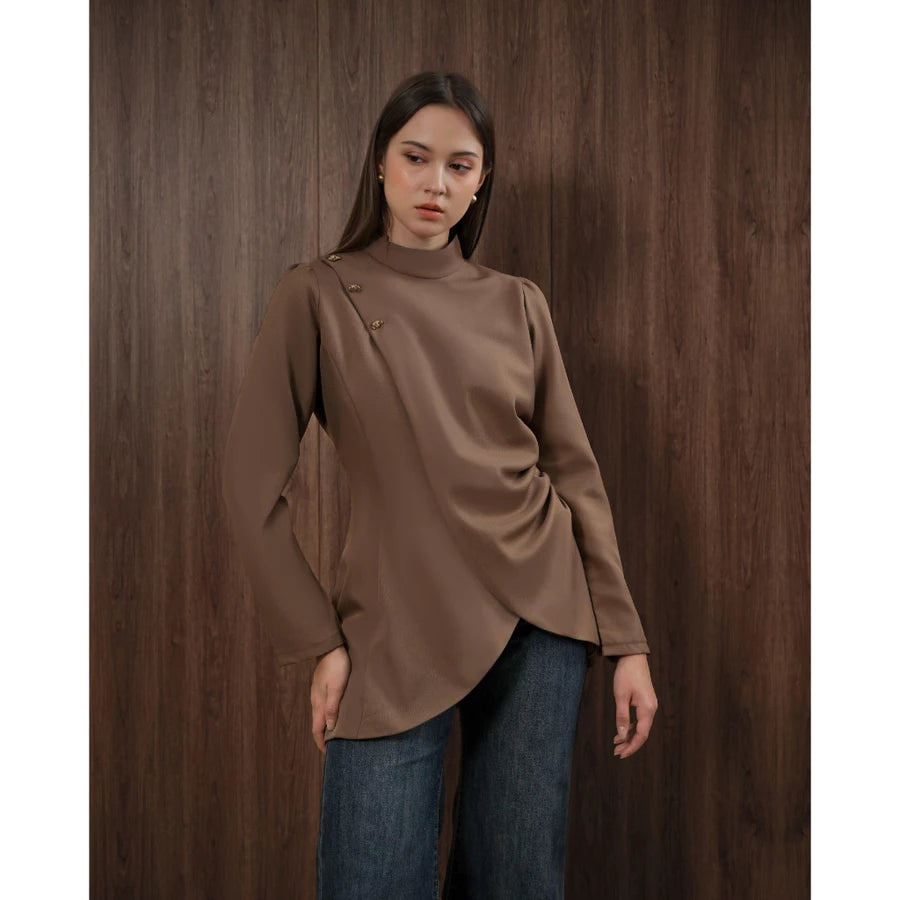 Woman wearing a brown blouse and blue jeans by Kasa Heritage against a wooden background